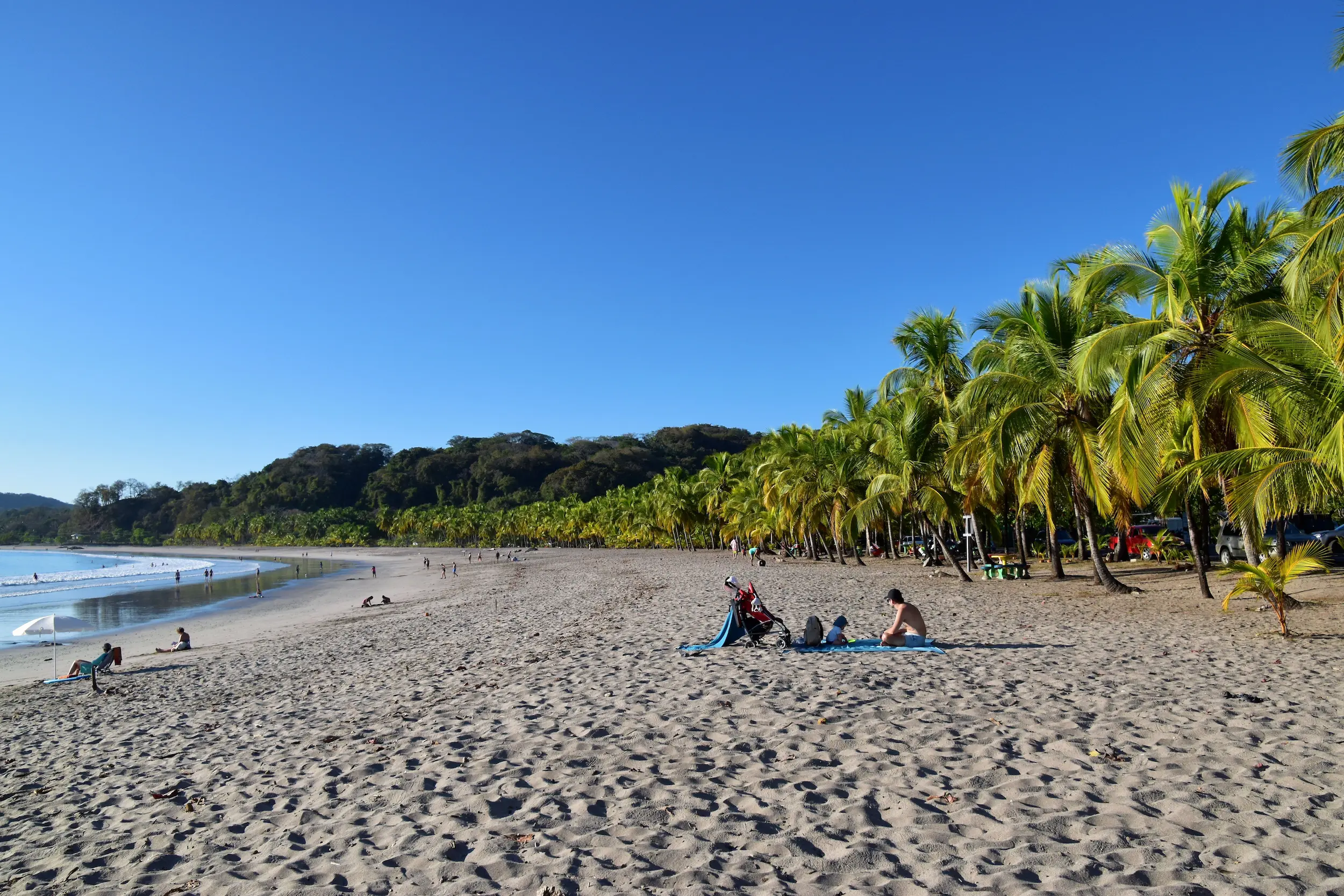 Family with a stroller relaxing under palm trees on Playa Carrillo beach, Costa Rica
